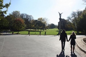 A couple walk hand in hand, and saunter through sunlight in Parc Montsouris